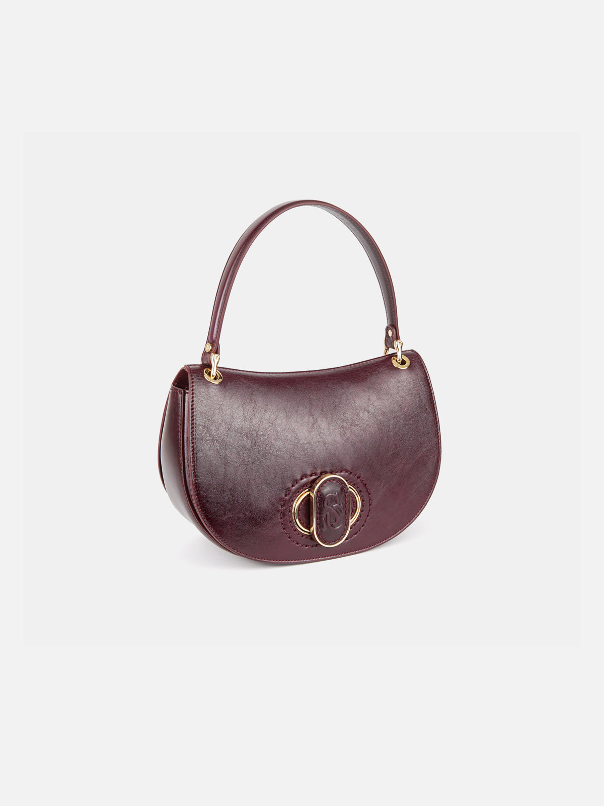 A dark burgundy leather saddle bag with gold-tone oval hardware on the front flap and a top handle, viewed from a three-quarter perspective.