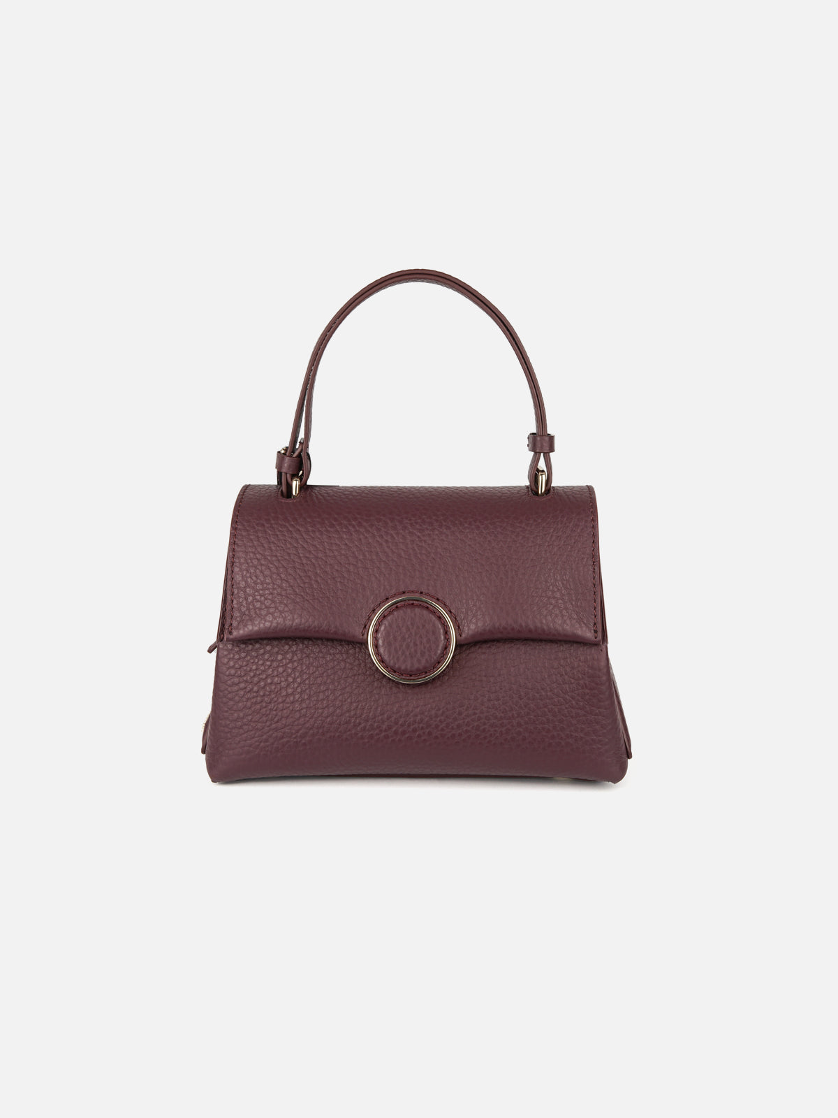 A frontal view of a luxurious, rich burgundy pebbled leather top-handle handbag, featuring a structured trapezoidal shape and a clean flap closure. The center is highlighted by a distinctive circular clasp buckle trimmed with a textured, polished gold hardware ring, presented against a minimalist off-white background.