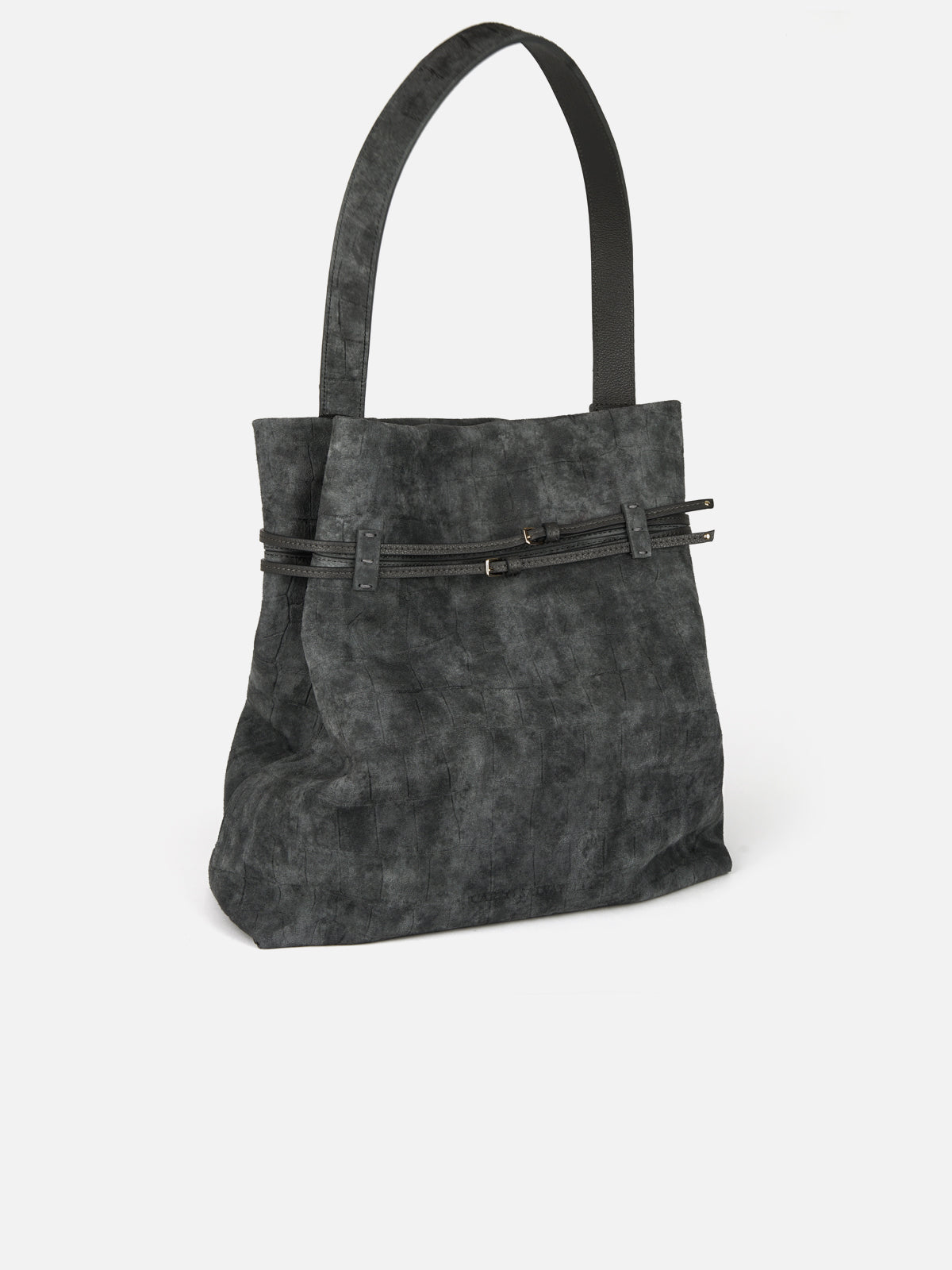 Three-quarter view of a tall, soft-structured shoulder hobo bag in charcoal grey distressed suede with a subtle embossed square texture. Features a wide flat shoulder strap, a relaxed slouchy body, and two thin black leather accent belts cinched around the middle with delicate gold buckles.